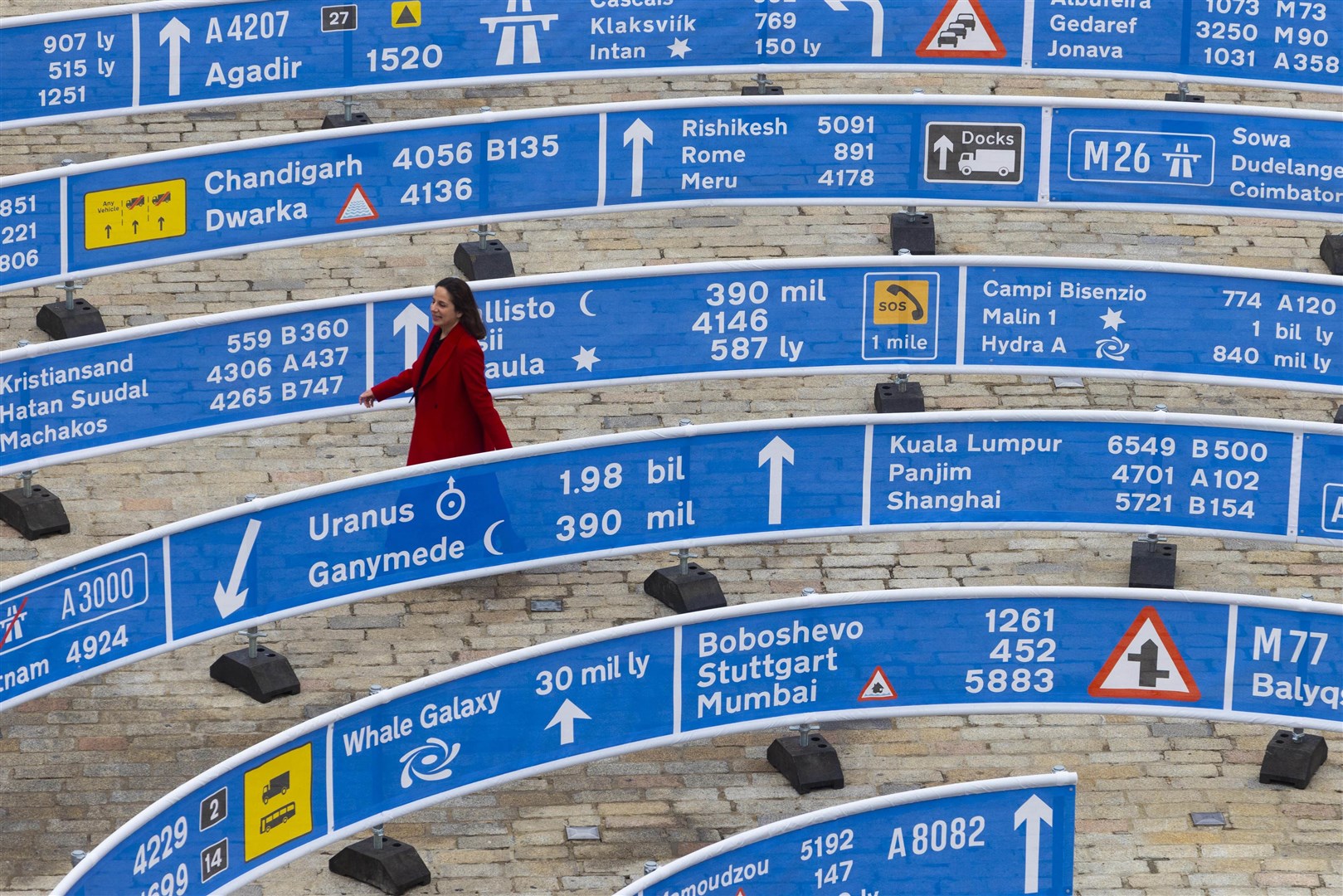 In a spiral shape, standing 336-metres (1,102-ft) long and 30-metres (98-ft) wide, the blue and white barriers have places, miles and traffic signs written on them. (David Parry/PA)