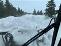A major road pile-up. Snow partially obstructs the view from the cabin of the piste basher clearing the road.