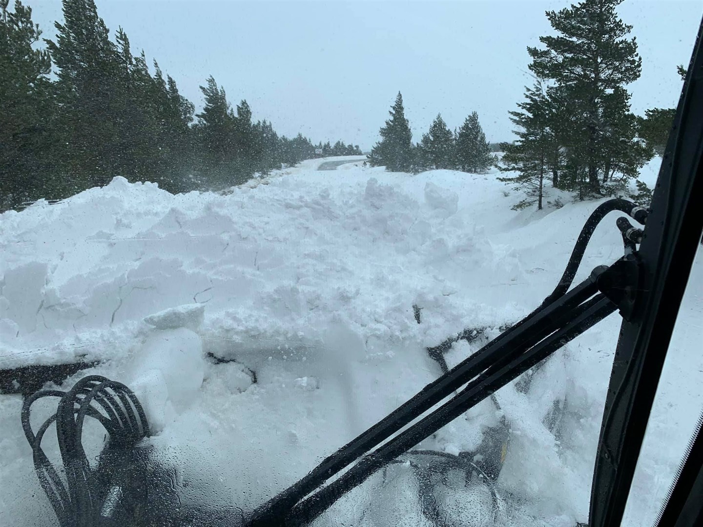 A major road pile-up. Snow partially obstructs the view from the cabin of the piste basher clearing the road.