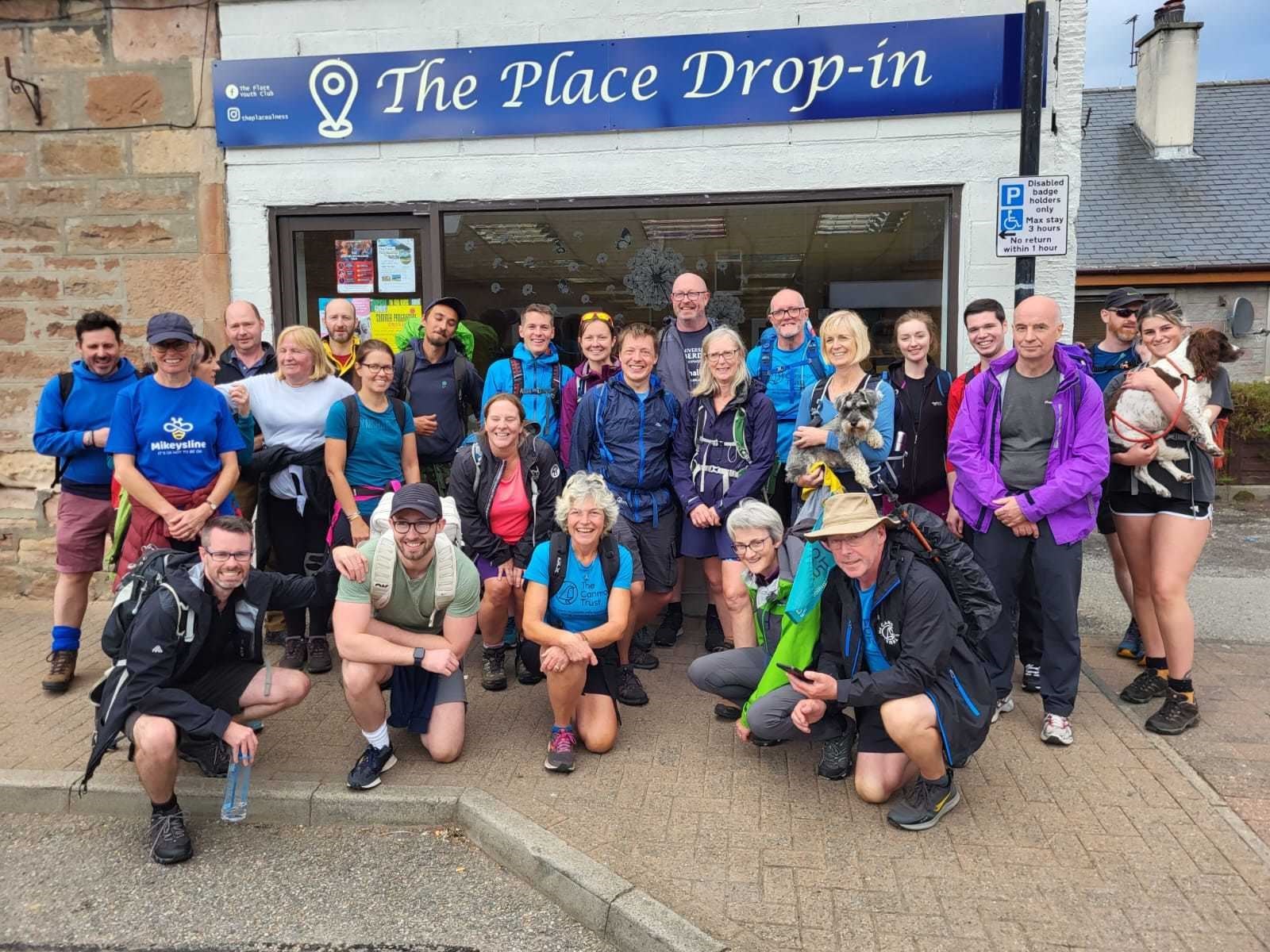 John Gibson of The Canmore Trust (crouching, front right) with Mikeysline and other supporters of mental health services outside The Place in Alness, where Mikeysline delivers support to the local community. John Gibson is featured in the latest episode of the podcast, Speaking of Suicide.