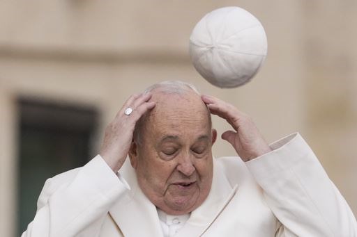 Pope Francis tries to catch his cap as wind blows it away while arriving for his weekly general audience in St Peter’s Square in 2024 (Andrew Medichini/AP)