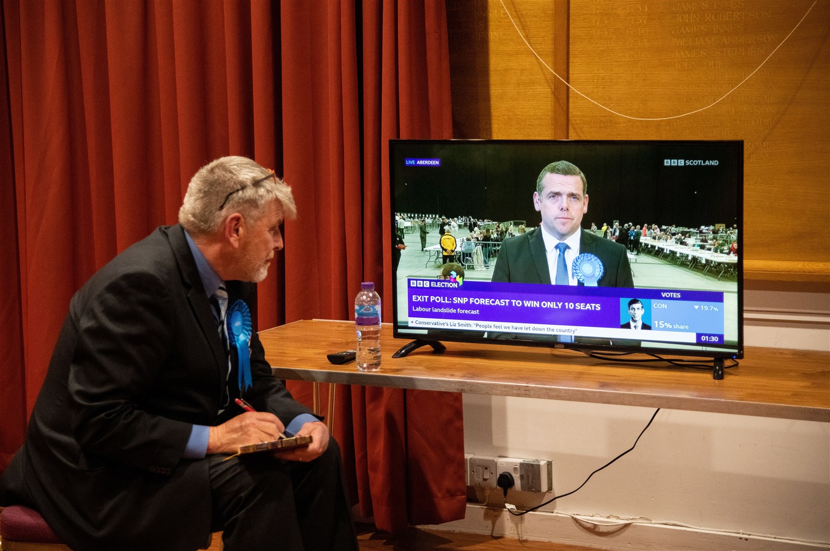 A Conservative watches on as Douglas Ross appears on the BBC's coverage. Moray West, Nairn and Strathspey Election Count at Elgin Town Hall. Picture: Daniel Forsyth.