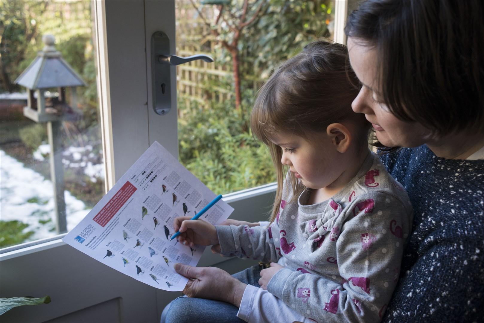 RSPB Big Garden Birdwatch. Mother and her daughter counting birds in their garden.