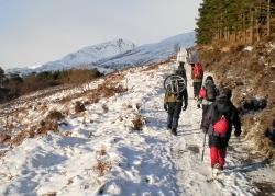 The group of rescuers walk in to the 'avalanche site' with rescue gear in and on their rucksacks.