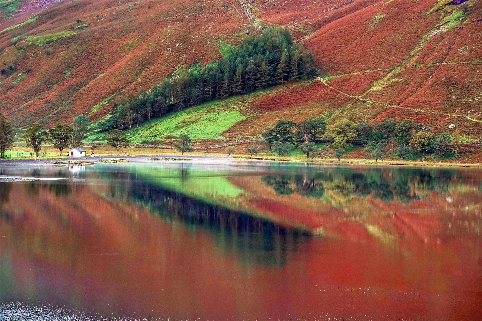Autumn colours are reflected in the water at Buttermere (Owen Humphreys/PA)