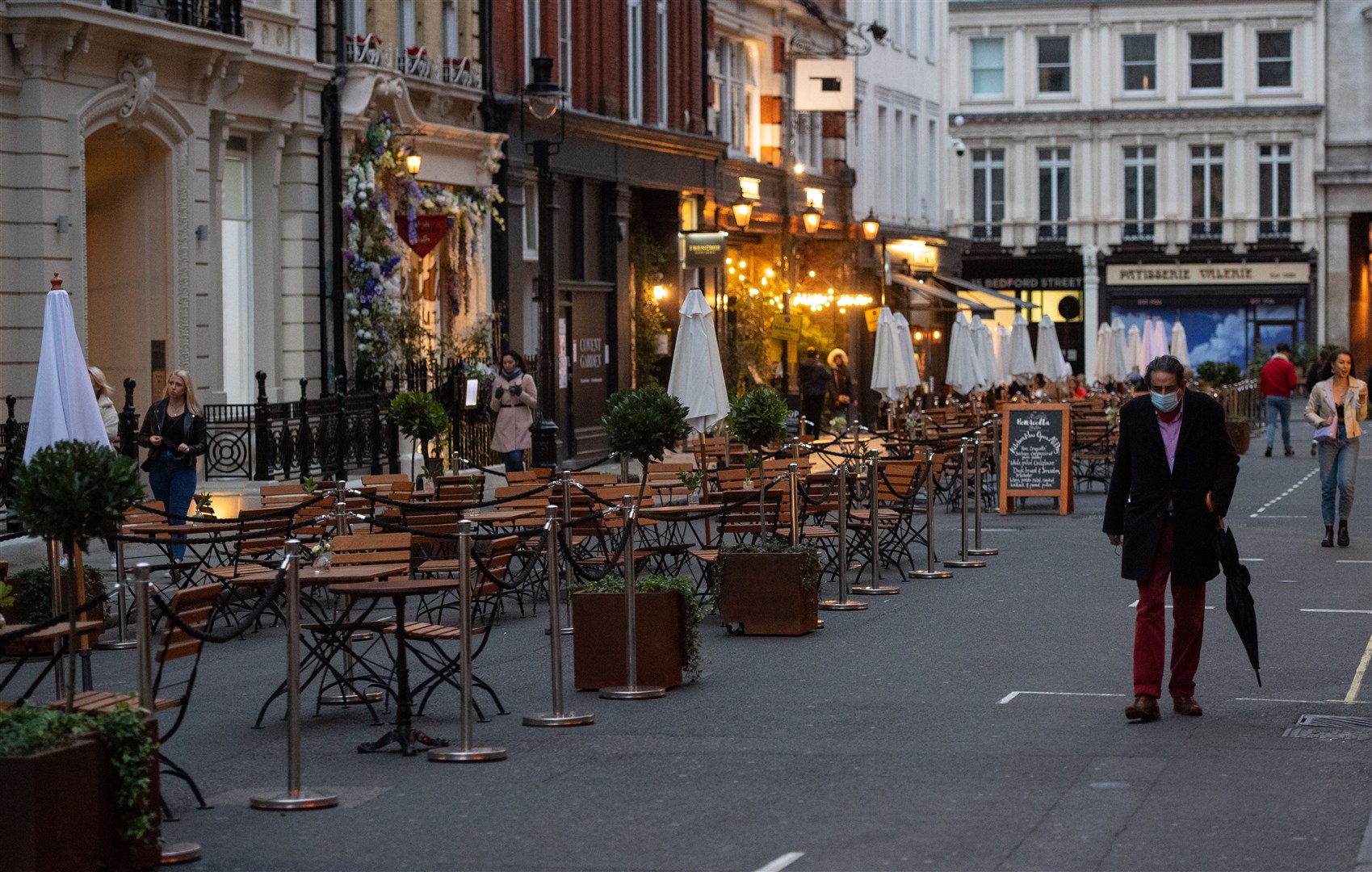 People pass empty tables outside a restaurant in London after the city was put into Tier 2 restrictions (Dominic Lipinski/PA)