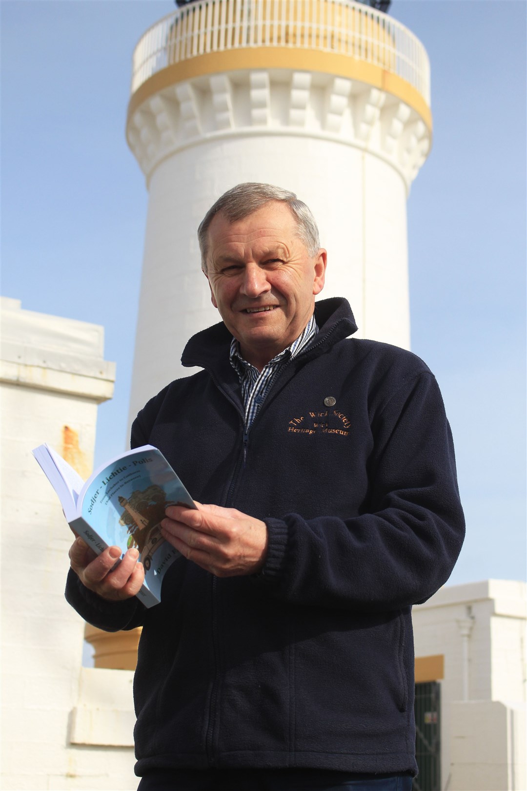 David Fraser at Noss Head lighthouse with a copy of his book, Sodjer – Lichtie – Polis. Picture: Alan Hendry