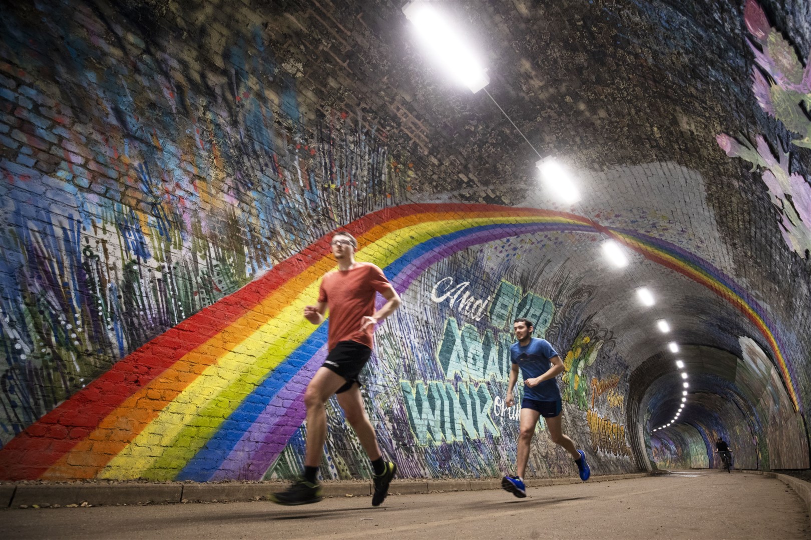 People taking their daily exercise pass underneath the rainbow mural in Colinton Tunnel, Edinburgh, as the UK continued in lockdown in April (Jane Barlow/PA)