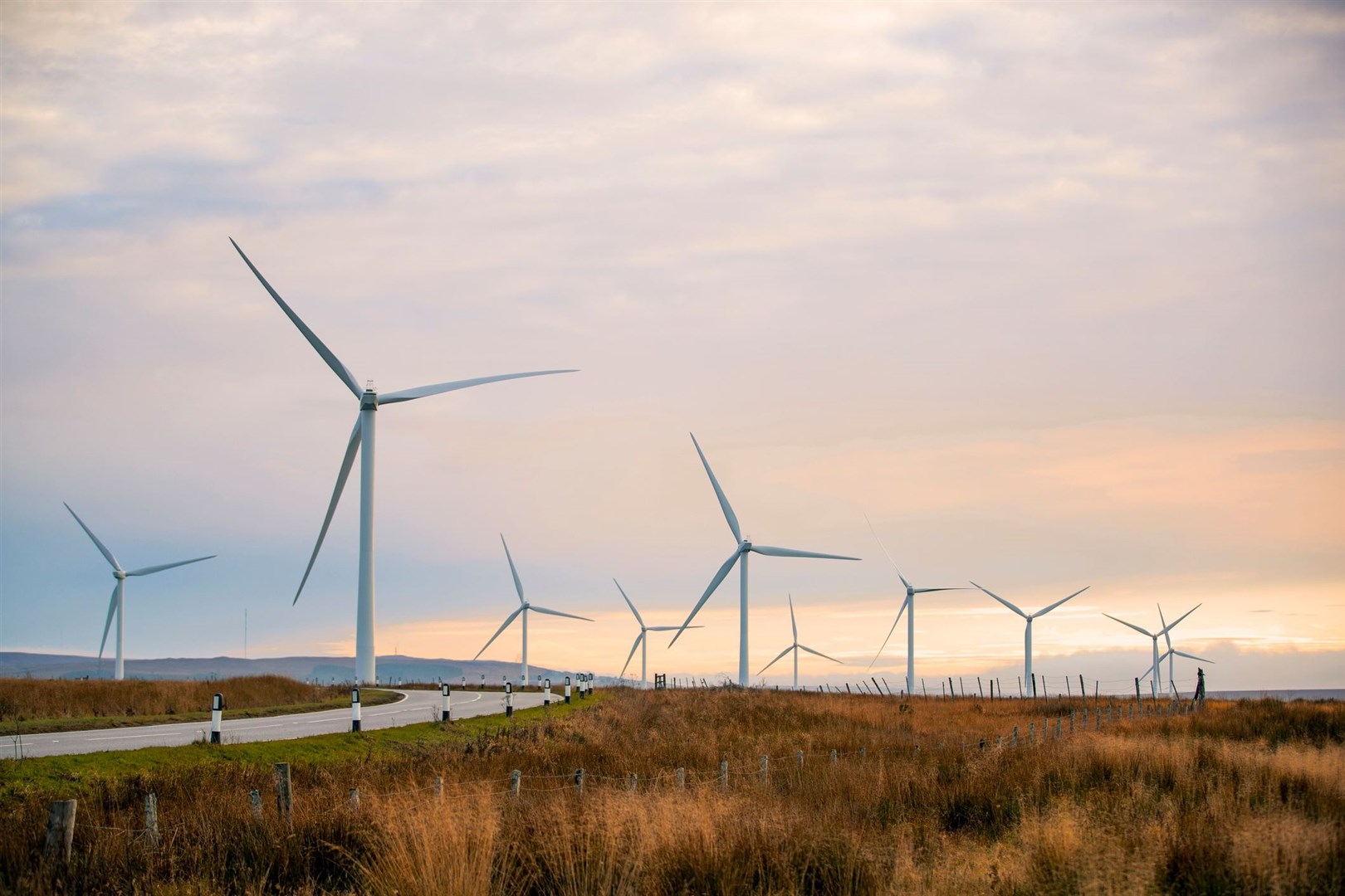 A sunset in the highlands with renewable energy wind turbines reaching far into the horizon.
