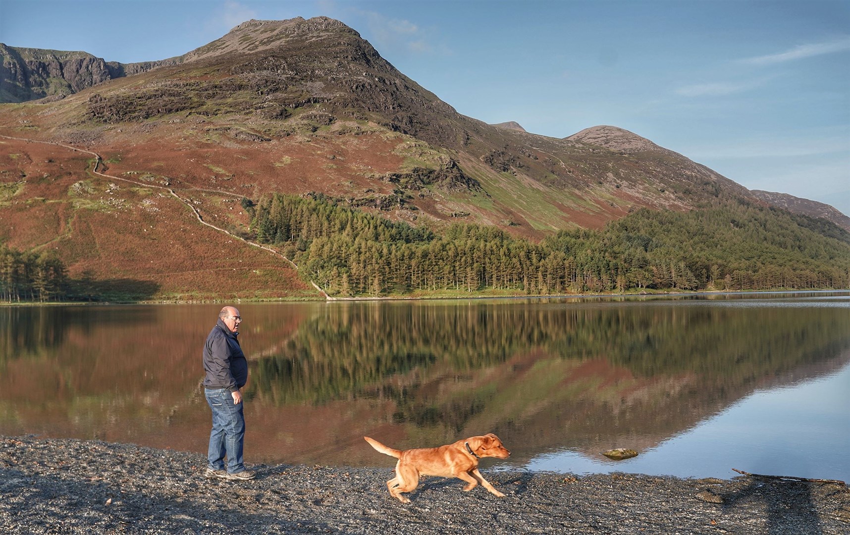 A man walking his dog at Buttermere in the Lake District (Owen Humphreys/PA)