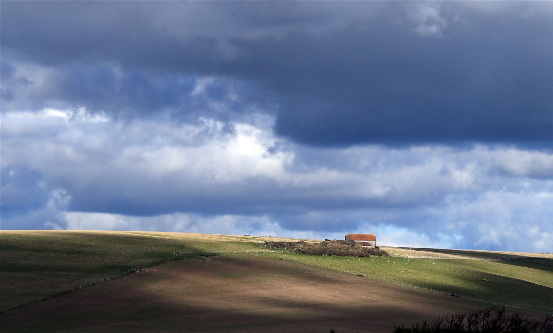 Farm buildings are bathed in light against the backdrop of a brooding sky on the South Downs near Eastbourne in Sussex (Gareth Fuller/PA)