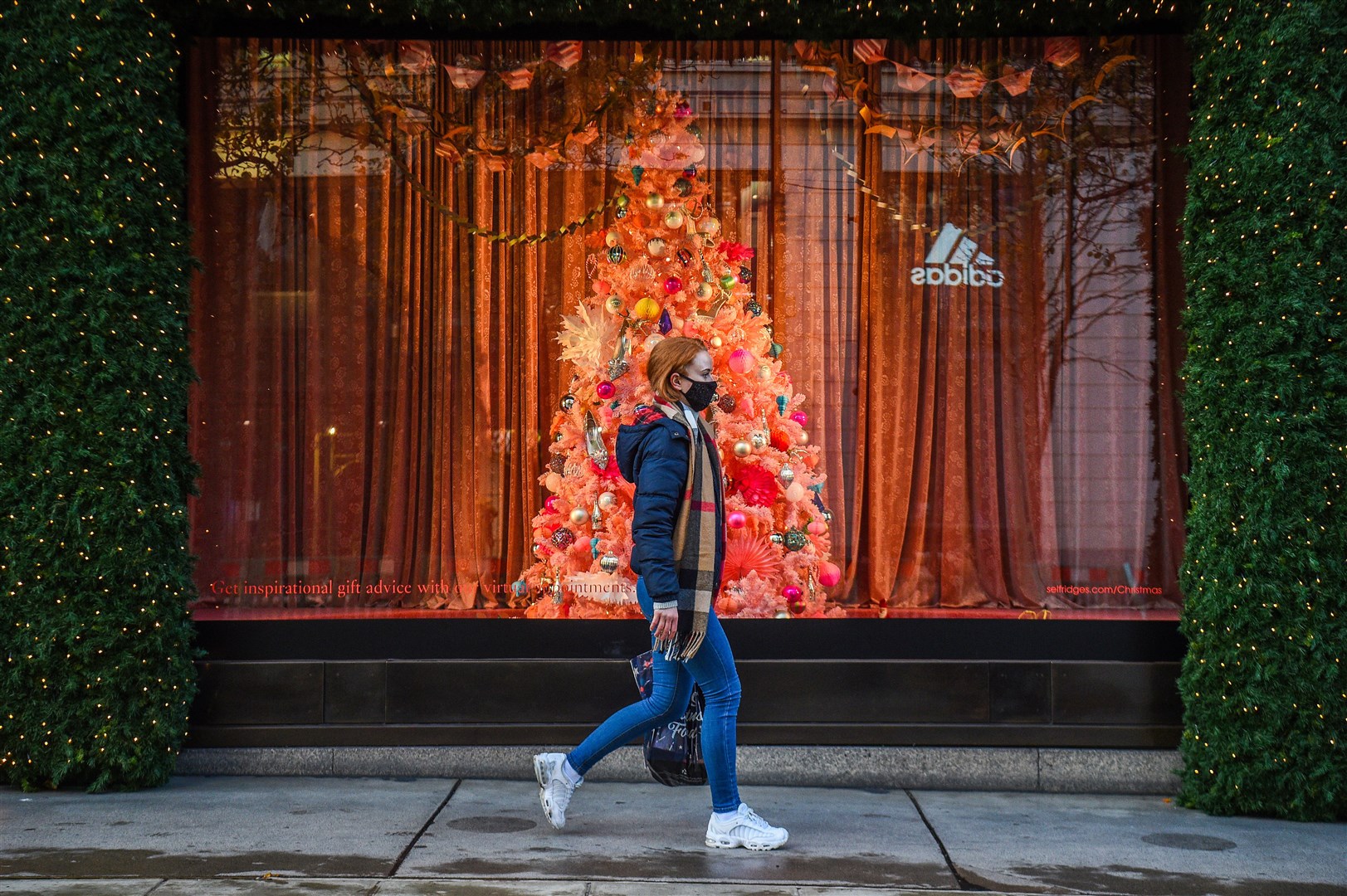 A woman wearing a face mask passes a Christmas window display on Oxford Street, London (Kirsty O’Connor/PA Images)