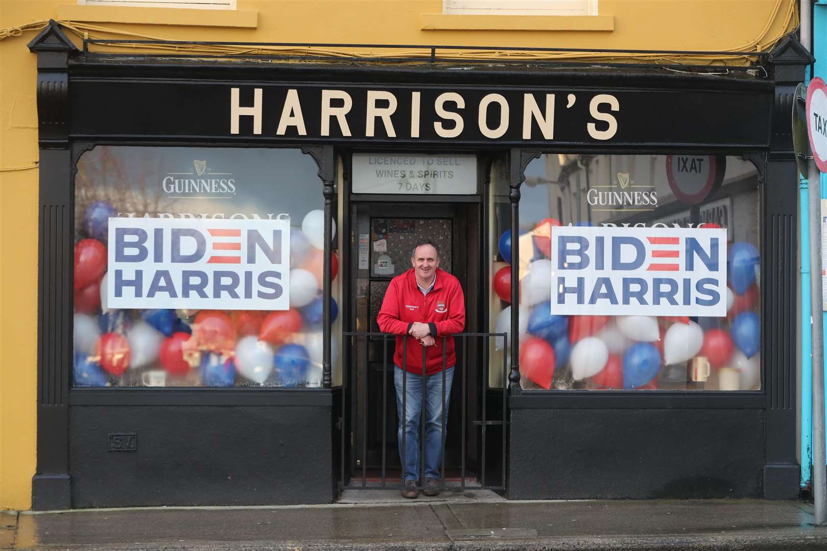 Derek Leonard stands in between his banner display for Joe Biden outside his pub Harrison’s, in Ballina (Niall Carson/PA)