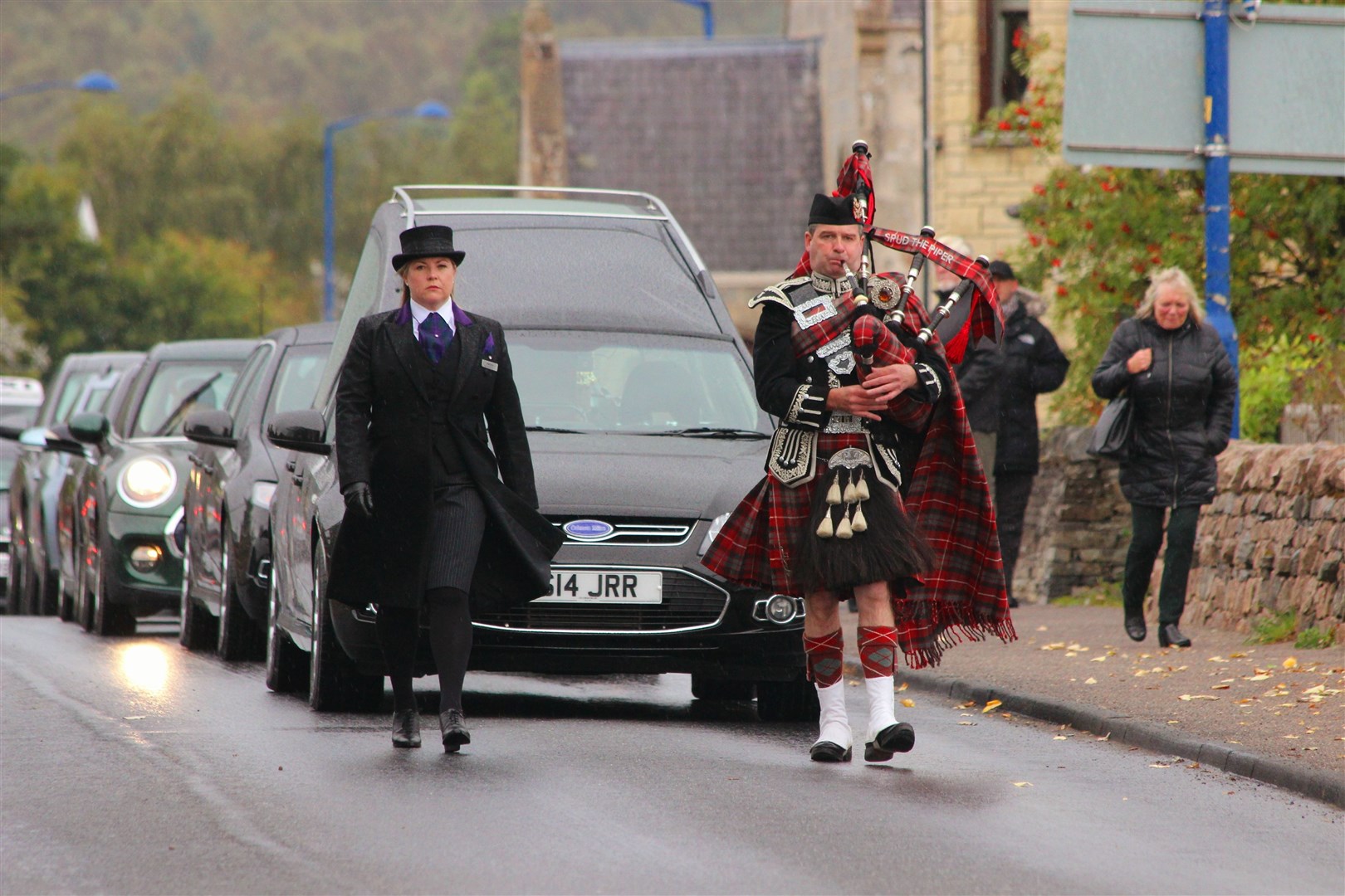 One Aviemore's musician's escort for another: Spud the Piper leads the funeral cortege through the village before its final departure for Inverness Crematorium this morning (David MacLeod)