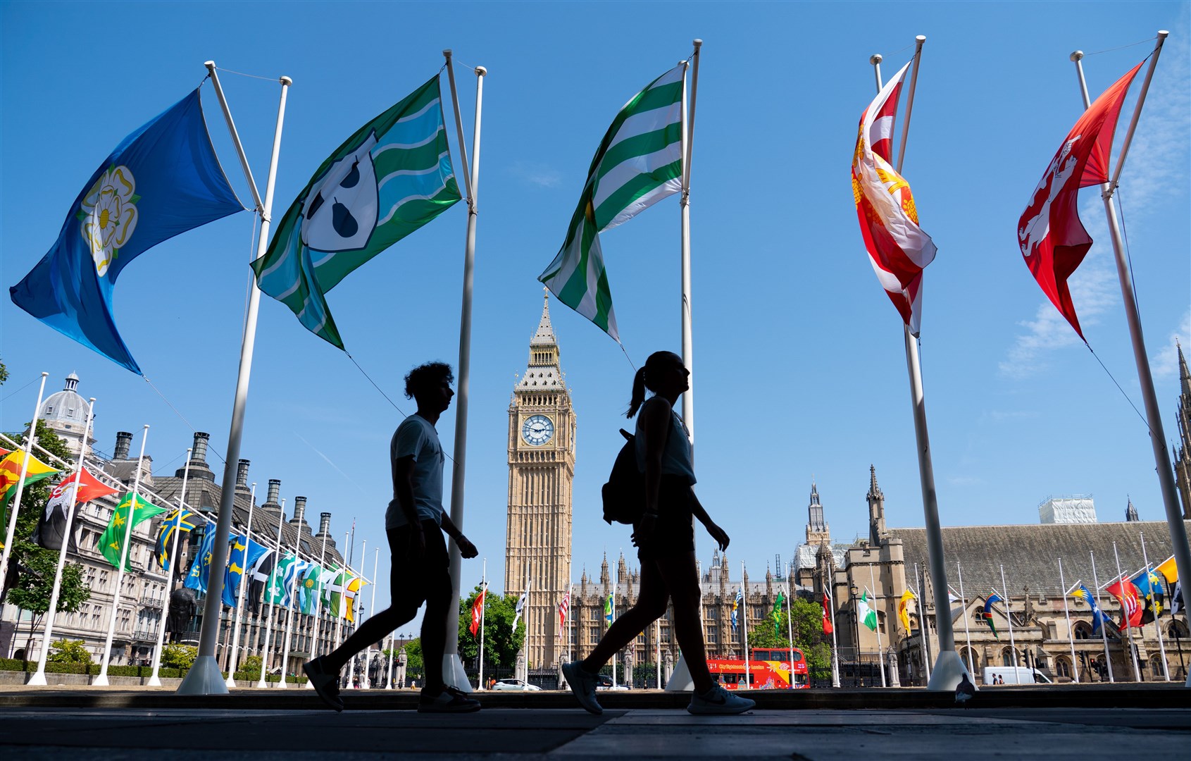People walk in the shade past national flags in Parliament Square, central London (Dominic Lipinski/PA)