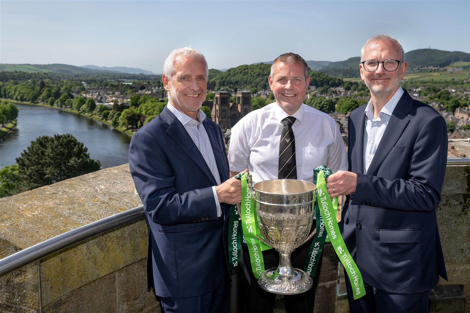 Tulloch Homes Managing Director Sandy Grant; Camanachd Association President Steven MacKenzie & Springfield Properties CEO Innes Smith with the Camanachd Cup atop Inverness Castle, overlooking Bught Park where the 2023 final will take place.