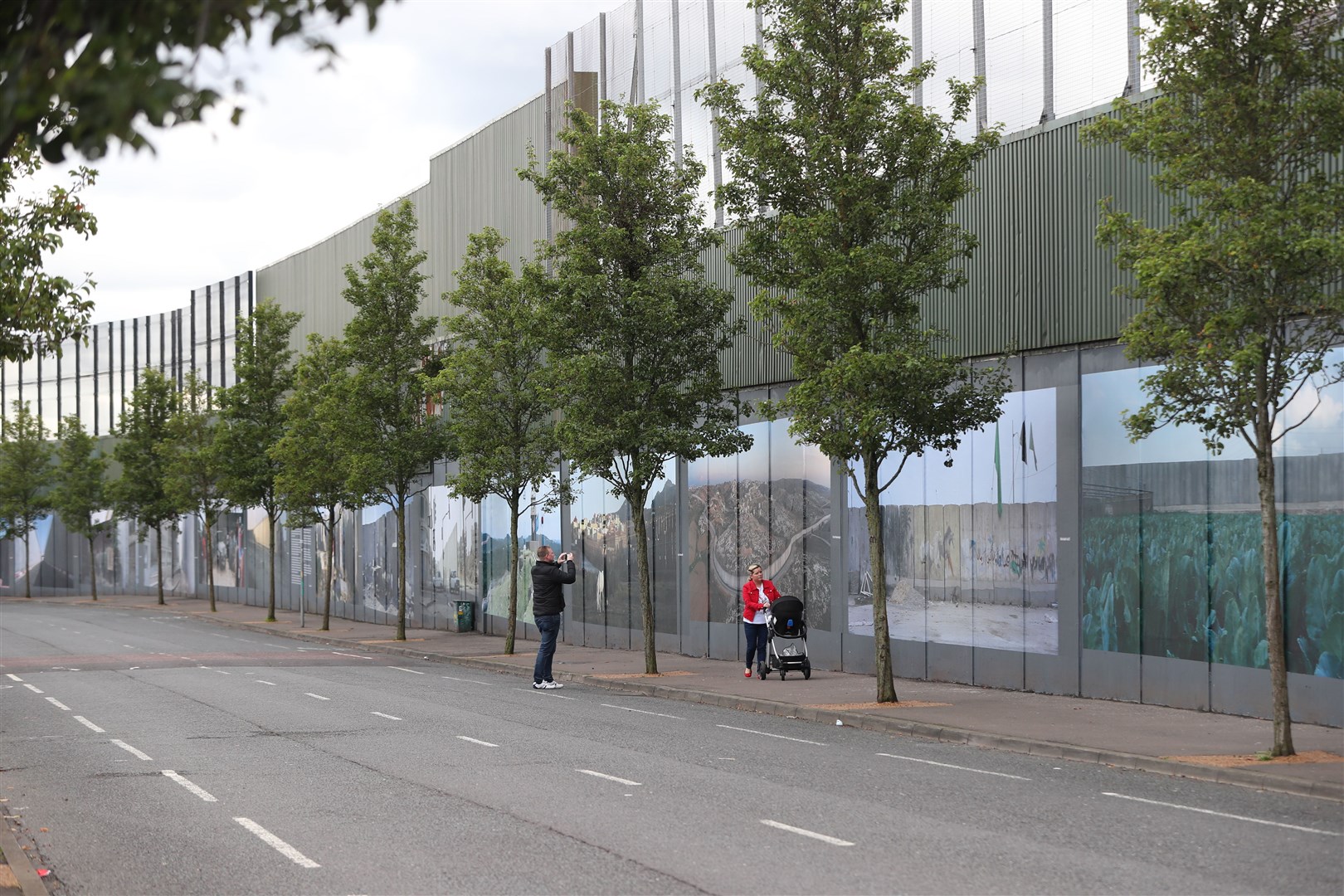 People walk past a peace wall in west Belfast that separates the unionist and nationalist communities in the area (Niall Carson/PA)