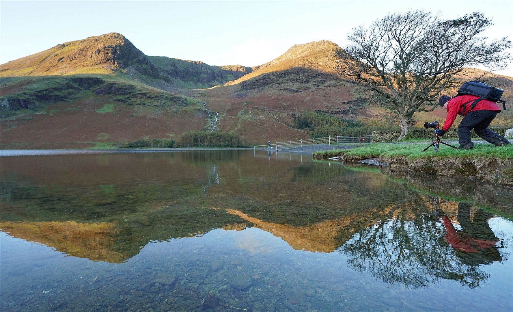 A photographer lines up his shot of autumn reflections at Lake Buttermere in the Lake District, Cumbria (Owen Humphreys/PA)