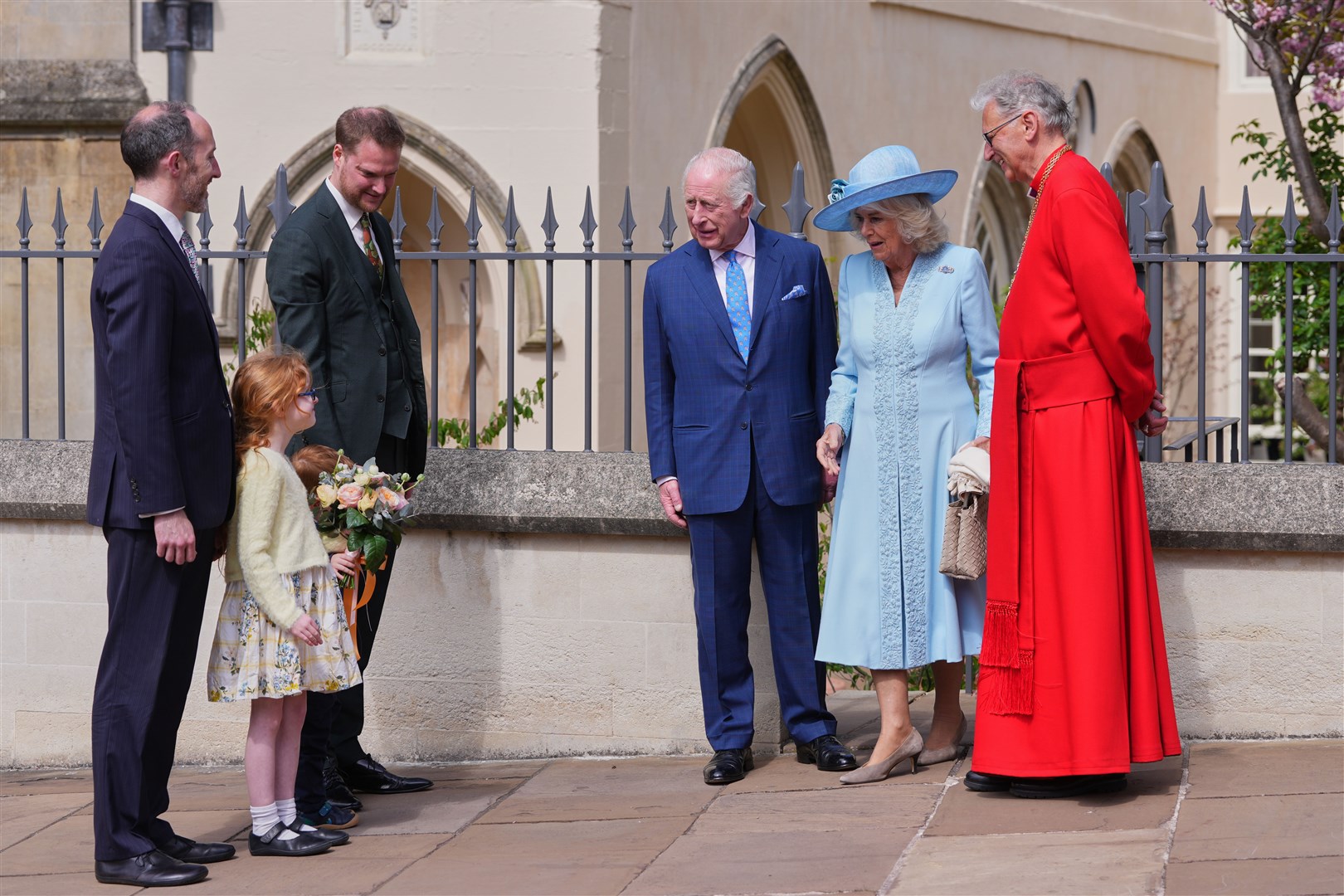 The Dean of Windsor, the Right Rev Christopher Cocksworth, stands with the King and Queen Camilla, as they look at a young girl who will present a posy (Kirsty Wigglesworth/PA)