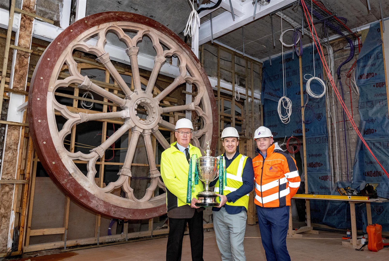 From left: Alister MacKinnon (Camanachd Association) presents the Camanachd Cup trophy to Michael Golding (High Life Highland) and Malcolm MacLeod (Highland Council) in front of the in-refurbishment Rose Window. Picture: Neil G Paterson